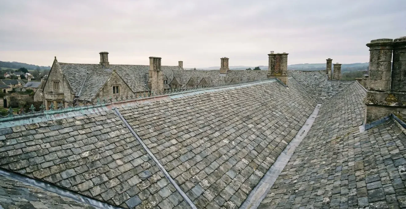 Vue rapprochée d'une toiture en ardoise d'un monument historique avec zinguerie en cuivre patiné sous lumière naturelle douce