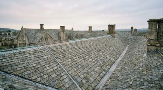 Vue rapprochée d'une toiture en ardoise d'un monument historique avec zinguerie en cuivre patiné sous lumière naturelle douce